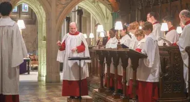 The Cathedral's Choristers, wearing white and red cassocks, stand in the medieval wooden Quire stalls ahead of a service.