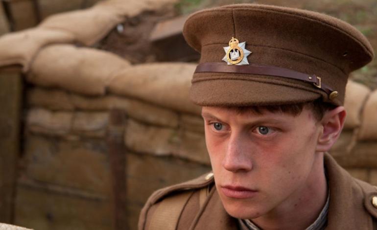 a man in a WW1 uniform standing in a trench looks worried